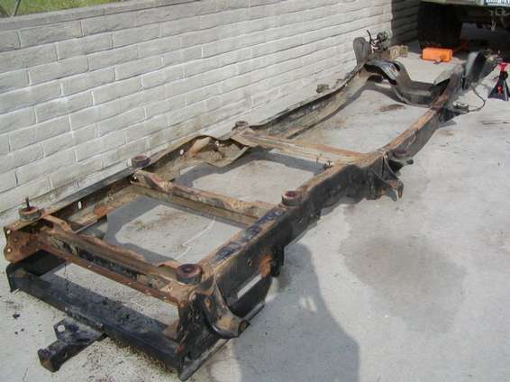 Rusty bare truck frame resting on a driveway against a brick wall