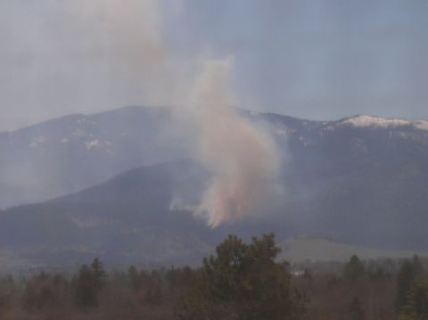 1996 Ford Bronco - A large plume of smoke billows from a mountainside, obscuring the view of the distant snow-capped peaks.