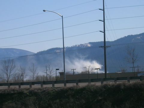 1996 Ford Bronco - A hazy scene unfolds with smoke rising from a distant hillside, framed by power lines and streetlights against a clear blue sky.