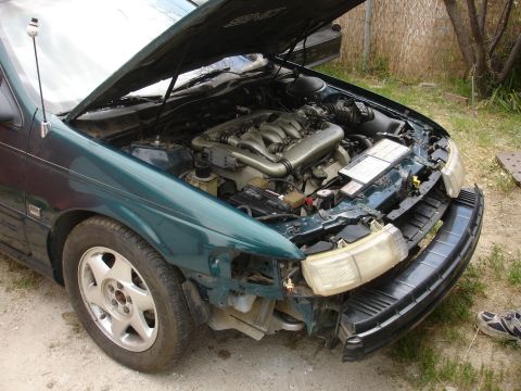 1995 Ford Taurus - Front end damage on a 1995 Ford Taurus, showing the engine with the hood up.