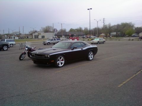 2000 Mercury Grand Marquis - A black Dodge Challenger is parked in a lot next to a motorcycle, with other vehicles and buildings in the background.