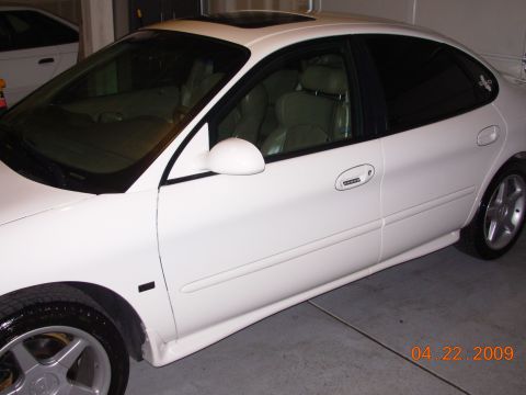 1995 Ford Taurus - Side view of a white sedan, parked indoors with another vehicle in the background.