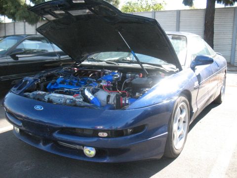 1995 Ford Probe - The front of a blue Ford Probe is shown with its hood open, revealing a modified engine and turbocharger.