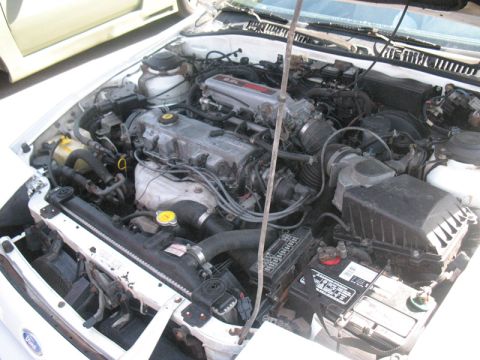 1995 Ford Probe - The engine compartment of a white car is shown with various mechanical components and wiring.