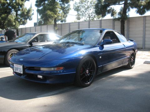 1995 Ford Probe - A blue 1995 Ford Probe is parked next to another car under trees.