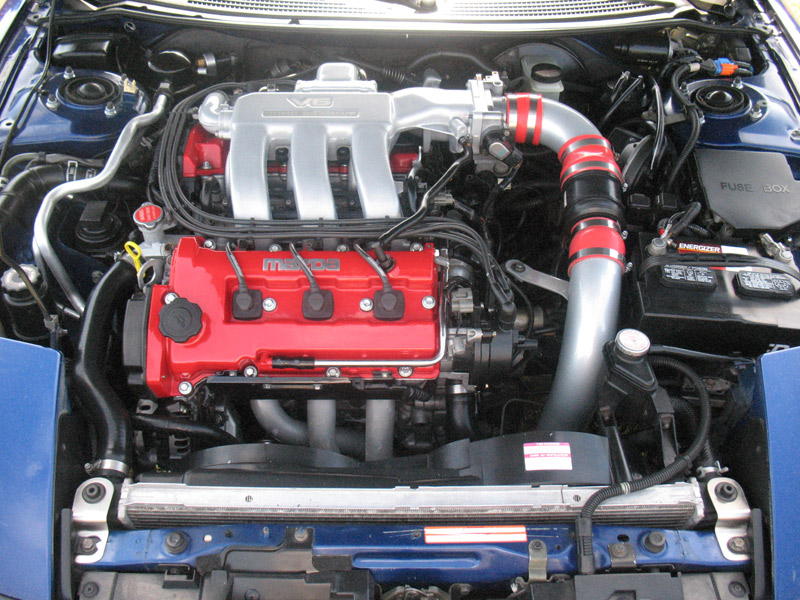 Mazda V6 engine bay with red valve covers, silver intake plenum and black cold-air intake tube