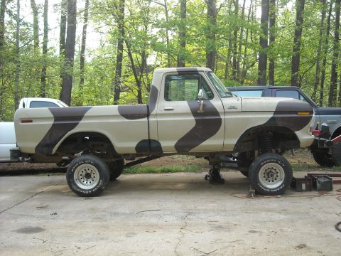 1979 Ford F-150 - Side view of a lifted pickup truck with camouflage paint, parked outdoors with trees in the background.