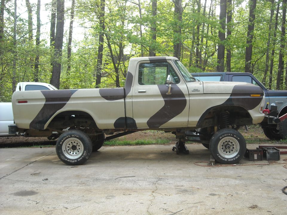 Tan and brown camouflage pickup truck, lifted, with aftermarket wheels, on jack stands