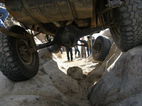 1989 Ford Bronco - An off-road vehicle is shown navigating a challenging rocky path, with its undercarriage and tires clearly visible.