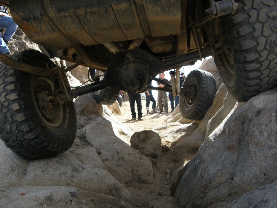Underside view of an off-road vehicle navigating a rocky terrain, with tires and suspension visible