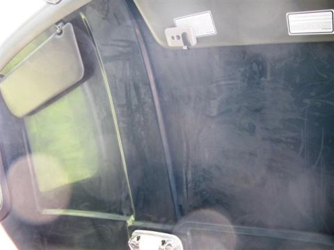 1992 Ford Bronco - The interior of a vehicle is shown, including a sun visor and a dusty dashboard with two labels on the ceiling.