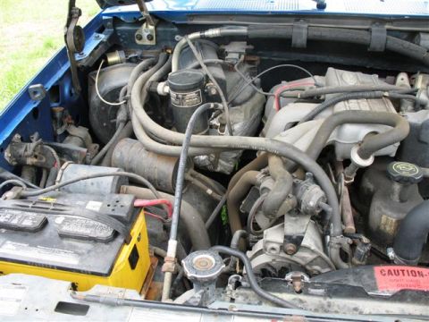 1992 Ford Bronco - The engine bay of a blue vehicle is shown, with various hoses and mechanical parts filling the frame.