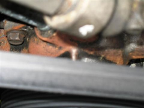 1992 Ford Bronco - Close-up of a rusty engine component with a bolt and a ribbed belt visible.