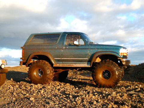 1996 Ford Bronco - A modified teal Ford Bronco sits on a rocky surface under a cloudy sky.