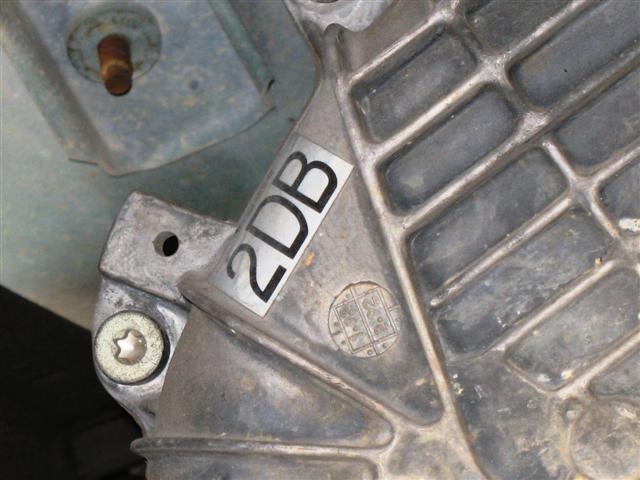 Close-up of a metal part with a sticker labeled '2DB' and a circular embossed symbol