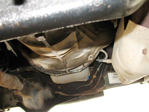 1992 Ford Bronco - The underside of a vehicle shows the transmission housing, exhaust system, and catalytic converter. A black metal frame is visible above th…