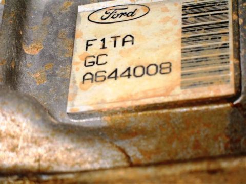 1992 Ford Bronco - Macro shot of a Ford part-identification barcode label reading 'F1TA GC A644008' with the blue Ford oval, still stuck to a rusty cast-metal…