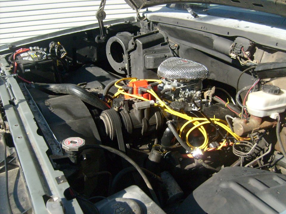 V8 engine bay with chrome air cleaner, orange distributor, and yellow plug wires