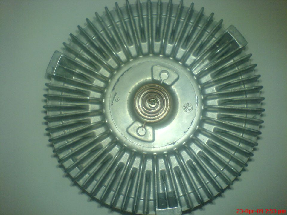 Silver metal fan clutch with radiating fins and a central coiled spring.