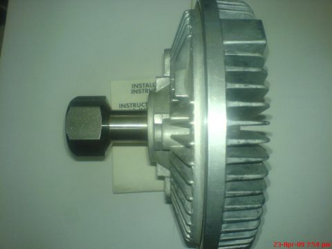 1992 Ford Crown Victoria - A close-up, side view of a silver fan clutch assembly with a hex nut on the shaft. A portion of an instruction manual is visible behind the…