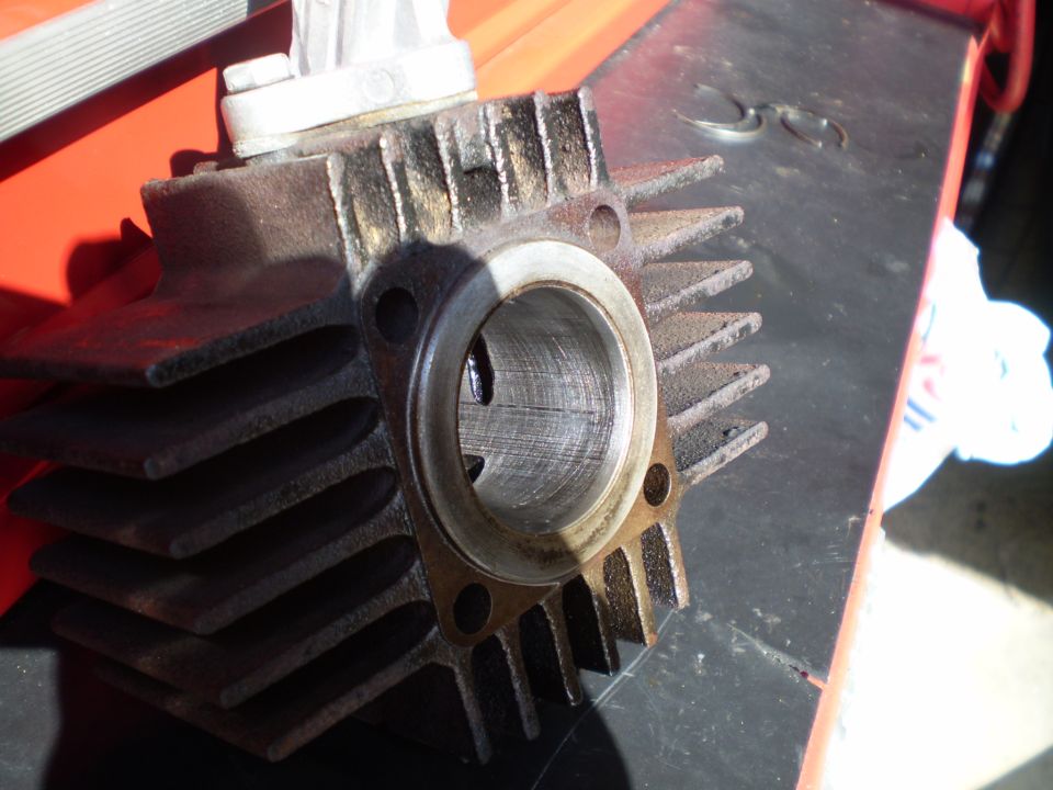 Removed two-stroke cylinder showing bore, ports and rusty cooling fins on a red toolbox