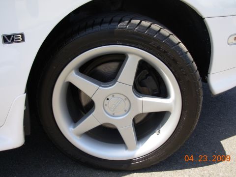 1995 Ford Taurus - Close-up of a white car's fender and wheel, showing a V8 badge and a silver five-spoke alloy wheel.