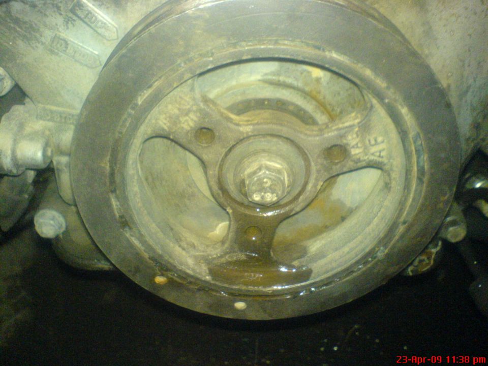 Close-up of a dirty crankshaft pulley with a central bolt and fluid leakage
