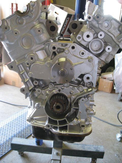 1994 Ford Probe - Close-up view of a silver engine block mounted on an engine stand, revealing internal components like timing gears and the water pump.