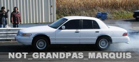 1997 Mercury Grand Marquis - A white 1997 Mercury Grand Marquis performs a burnout on a track, kicking up smoke.