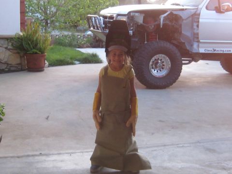 1996 Ford Bronco - A young girl dressed in protective gear stands before a heavily modified truck, possibly undergoing repairs or customization.