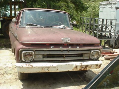 1962 Ford F-100 - This vintage Ford truck shows significant wear and tear, with a prominent grille and faded paint.