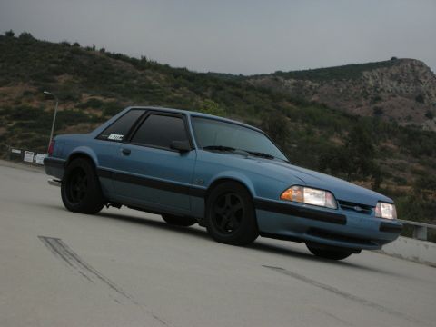 1990 Ford Mustang - A blue coupe is parked on a road with tire marks visible on the pavement.