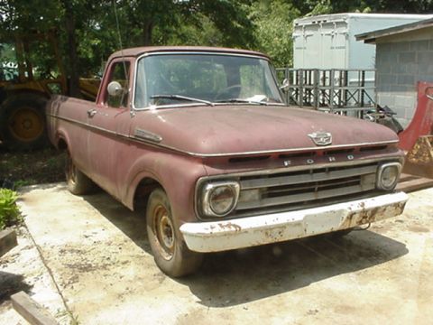 1962 Ford F-100 - A weathered 1961 Ford F-100 pickup truck sits outdoors, its grille and front end visible.