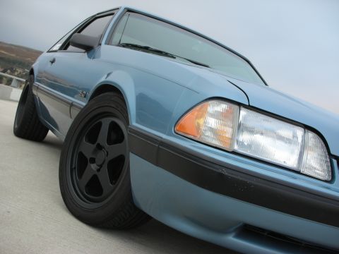1990 Ford Mustang - A light blue 1990 Ford Mustang is parked outdoors, showing its front quarter panel and wheel.