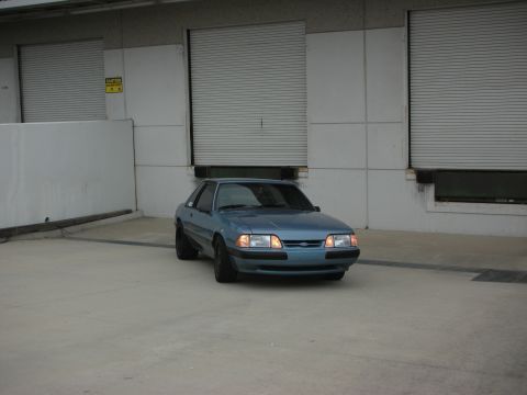 1990 Ford Mustang - A blue coupe sits in front of large, closed garage doors.