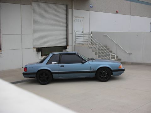 1990 Ford Mustang - Side view of a blue 1990 Ford Mustang coupe with aftermarket wheels and a sticker on the window.