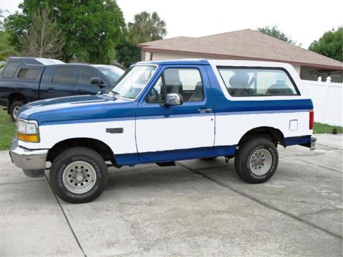 1992 Ford Bronco - Driver's-side profile of a fifth-generation Ford Bronco in blue over white with blue lower trim, parked on a concrete driveway in front of…