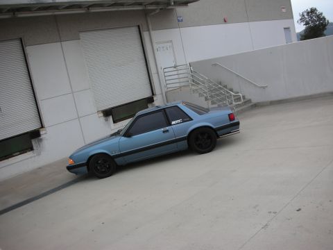 1990 Ford Mustang - A blue 1990 Ford Mustang is parked in front of a loading dock with a metal staircase nearby.