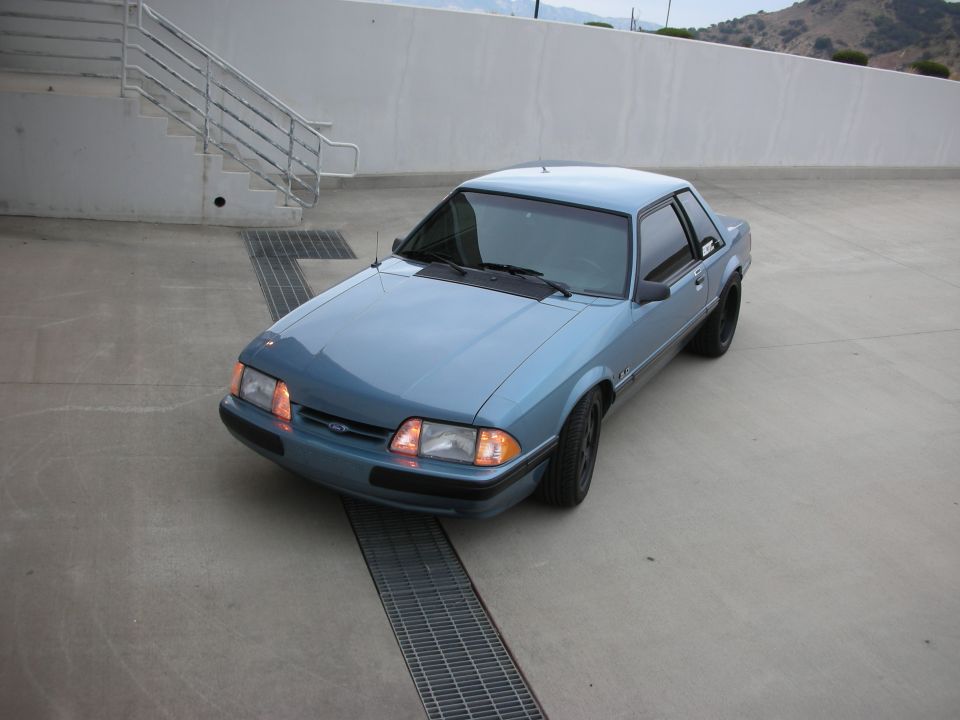 Blue coupe parked on concrete with metal grate in front. Side view shows black wheels and tinted windows