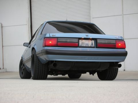 1990 Ford Mustang - The rear of a blue Ford Mustang is shown, with its distinctive taillights and "Mustang" badging visible.