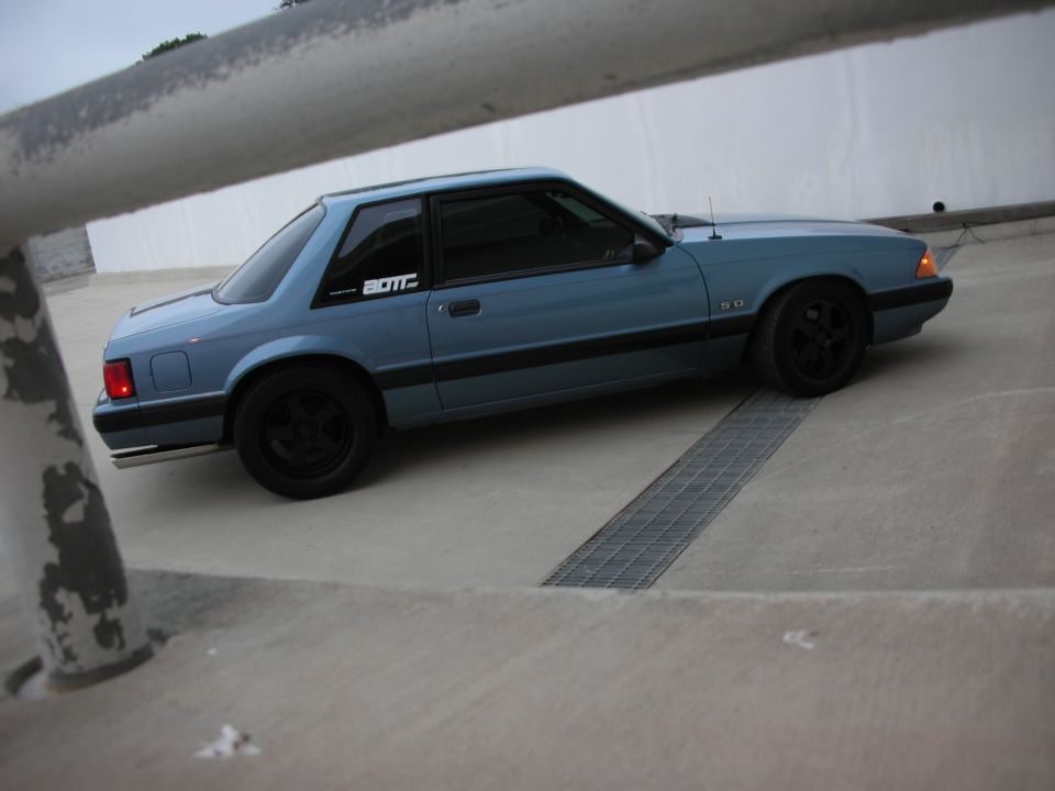 Blue 1990 Ford Mustang coupe with black wheels and a "5.0" badge