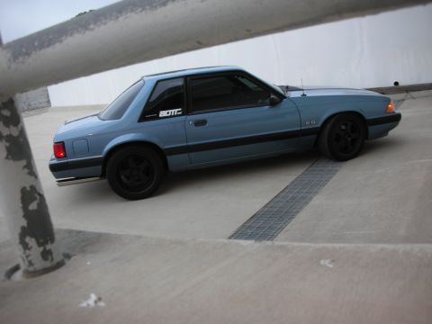 1990 Ford Mustang - A blue 1990 Ford Mustang coupe is parked on a concrete surface, viewed from the front three-quarter angle.