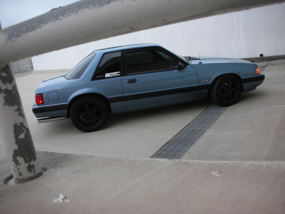 Blue 1990 Ford Mustang coupe with black wheels and a '5.0' badge on the fender