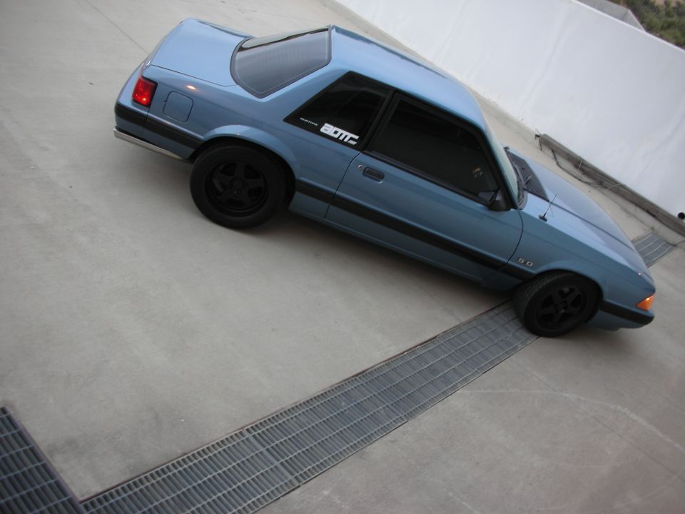 Blue coupe car with black wheels parked on concrete with metal grates