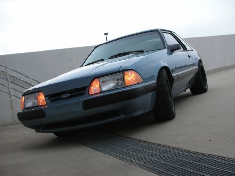 1990 Ford Mustang - A blue coupe is parked on a concrete surface, angled towards the viewer.