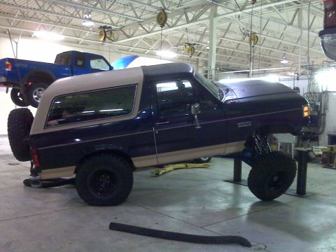 1990 Ford Bronco - Ford Bronco undergoing modifications in a garage, with a blue pickup truck also visible on a lift.