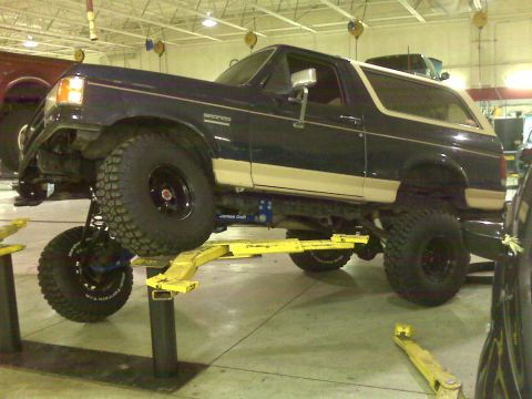 1990 Ford Bronco - A Ford Bronco is elevated on a hydraulic lift in a garage, revealing its modified suspension and off-road tires.