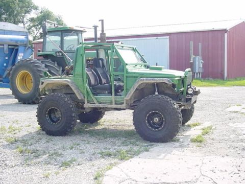 1992 Ford Bronco - A heavily modified off-road vehicle sits in a gravel lot beside a large green tractor and a red barn.