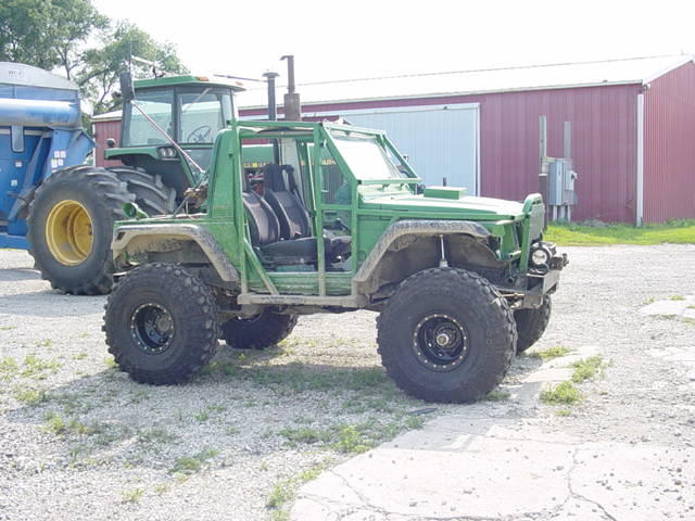 Green custom off-road vehicle with large tires parked next to a tractor