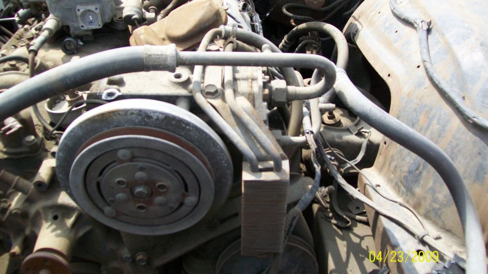 Close-up of engine components, including a pulley and hoses. Watermark says SUPERMOTORS.NET